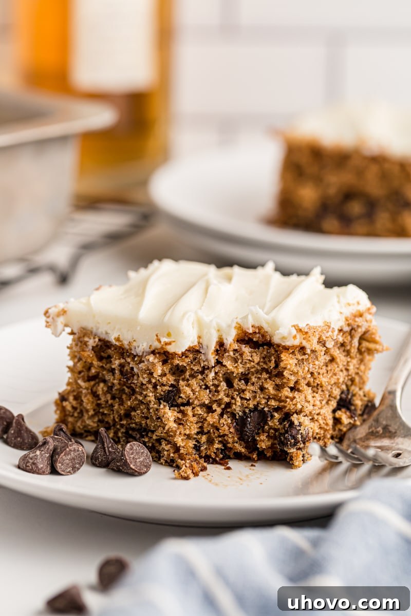 A slice of Oatmeal Chocolate Chip Cake on a plate, showing its moist texture, oats, and chocolate chips, topped with rich cream cheese frosting.