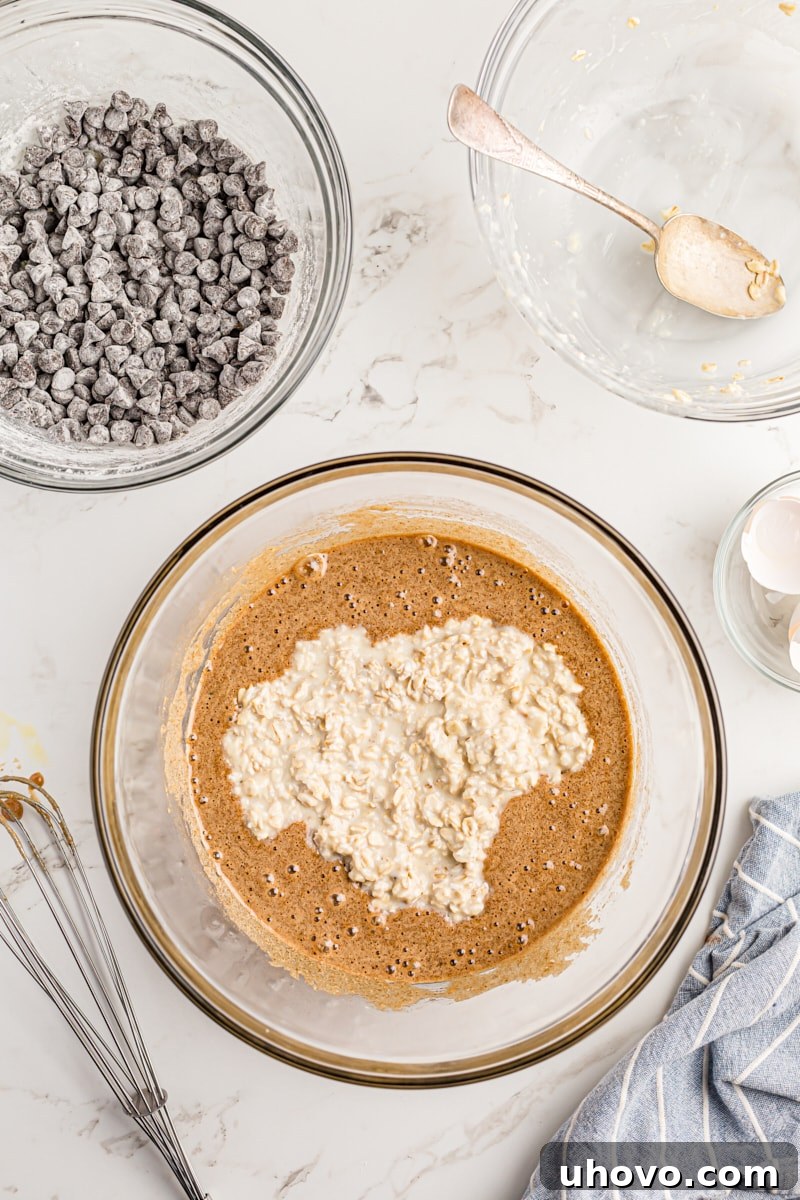 Overhead view of the softened oat mixture being folded into the wet ingredients in a large mixing bowl.