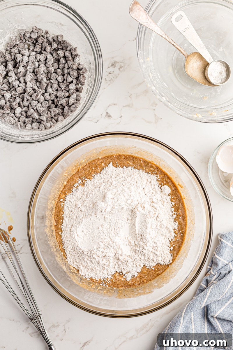 Overhead view of dry ingredients (flour, leavening) being added to the cake batter in a mixing bowl.