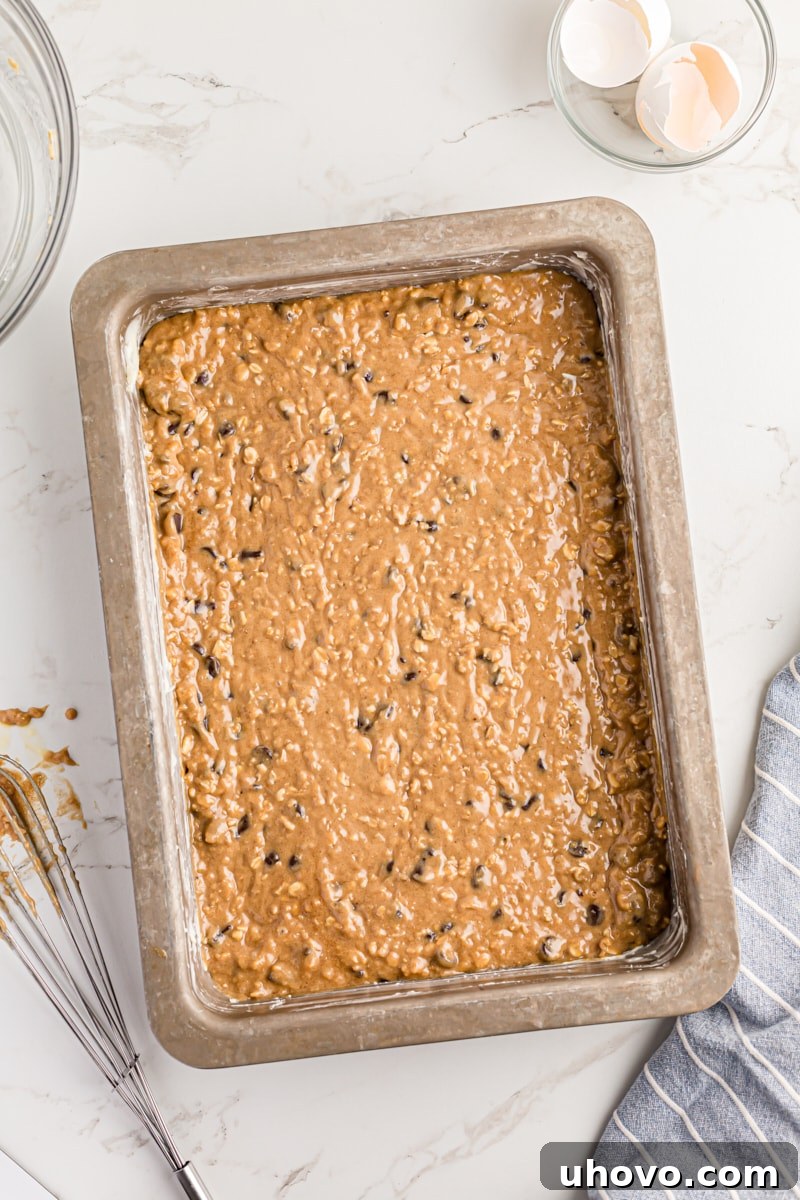 Overhead view of the oatmeal chocolate chip cake batter evenly spread in the greased metal baking pan.