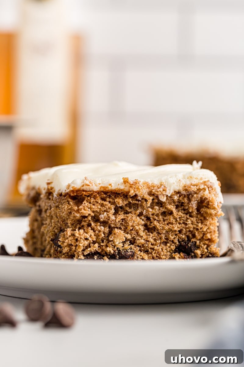 A perfectly baked and frosted slice of Oatmeal Chocolate Chip Cake, showcasing the fluffy cream cheese topping and a moist interior.