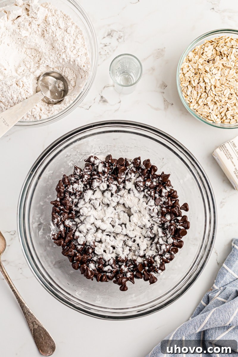 Overhead view of flour being sprinkled over chocolate chips in a mixing bowl.