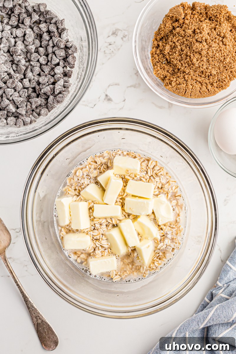 Overhead view of boiling water poured over butter and oats in a mixing bowl, beginning the softening process.