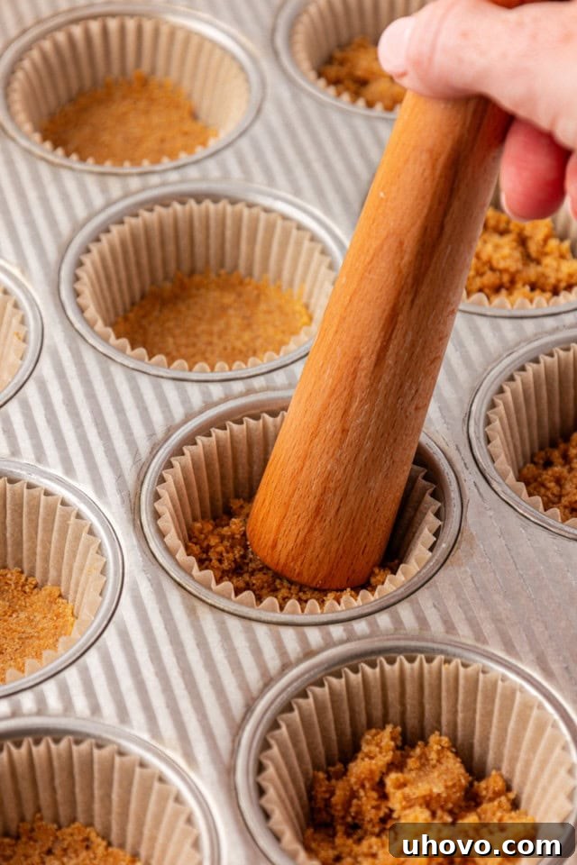 graham cracker crust being pressed into lined muffin pans