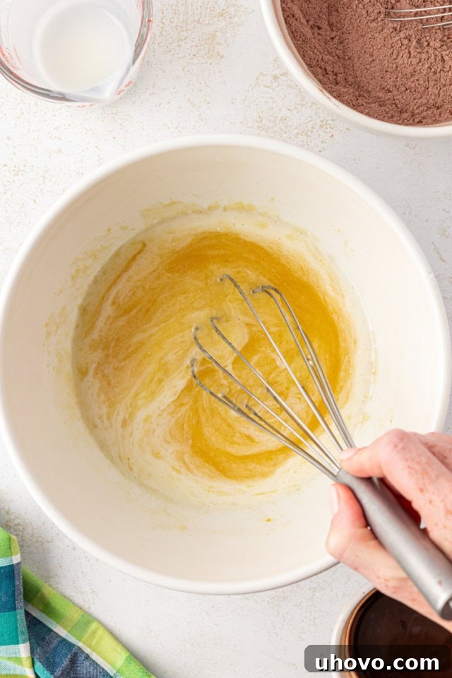 overhead view of melted butter, sugar, eggs, and vanilla being whisked together in a white bowl
