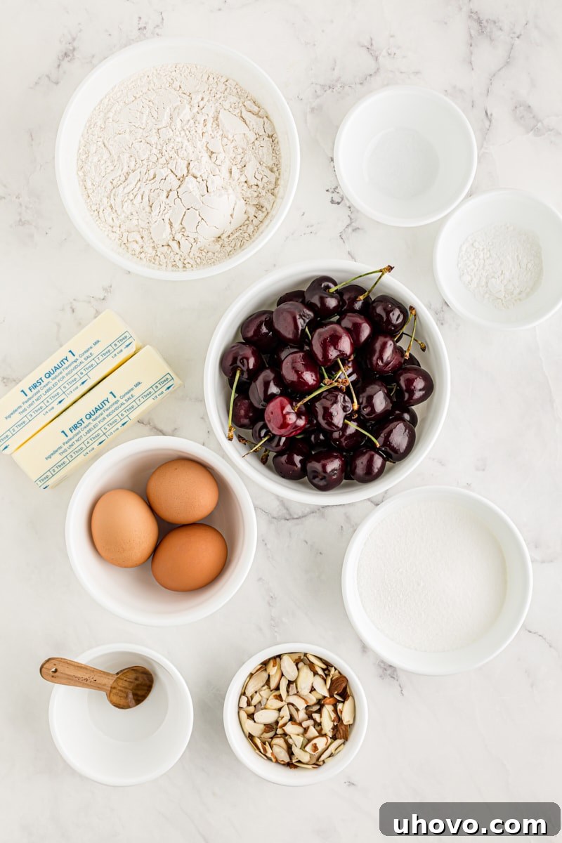 An overhead shot showcasing an array of fresh ingredients for the cherry almond sheet cake laid out on a clean surface, including flour, sugar, eggs, butter, cherries, and almonds, ready for baking.