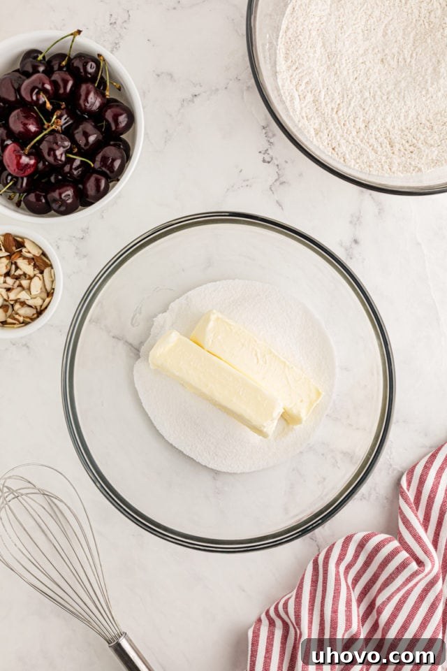 A close-up, overhead perspective of softened butter and granulated sugar combined in a clear glass bowl, showcasing their fluffy, pale yellow texture after being creamed together, a crucial step in cake making.