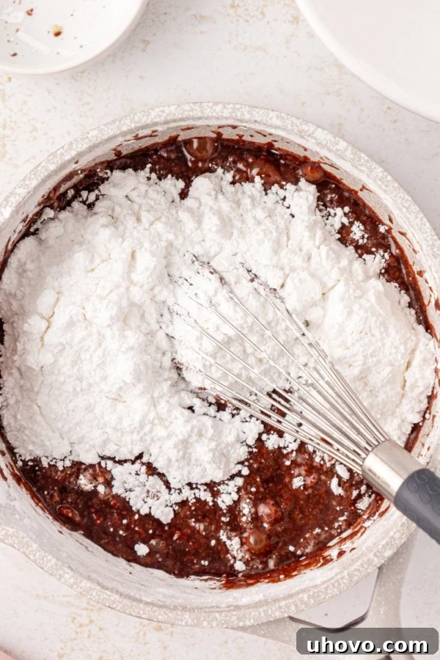 Confectioners' sugar, fragrant vanilla, and a pinch of salt are vigorously whisked into the warm butter, milk, and cocoa mixture, creating a smooth and glossy fudge frosting. Chopped nuts may also be added here.