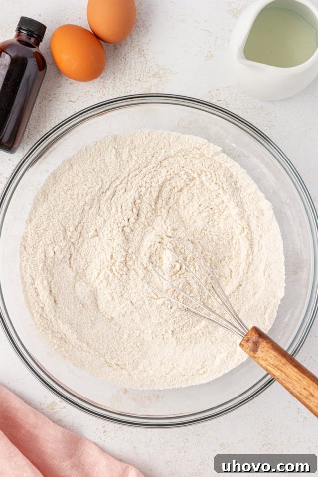 A glass mixing bowl holds the perfectly combined dry ingredients: granulated sugar, all-purpose flour, baking soda, and salt, ready for the wet components.