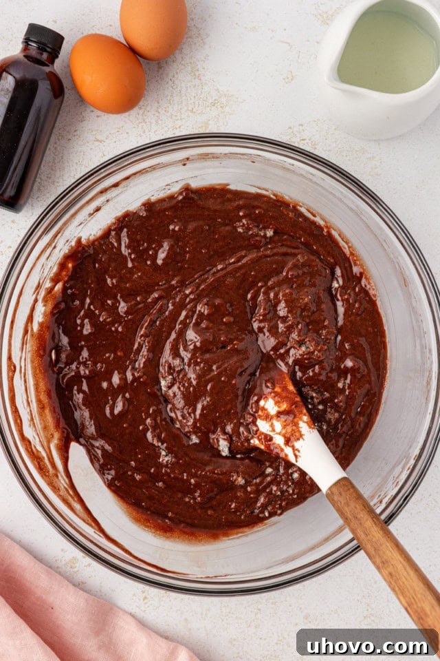 The hot cocoa mixture is being poured into the dry ingredients in a large mixing bowl, beginning to form the rich chocolate cake batter.