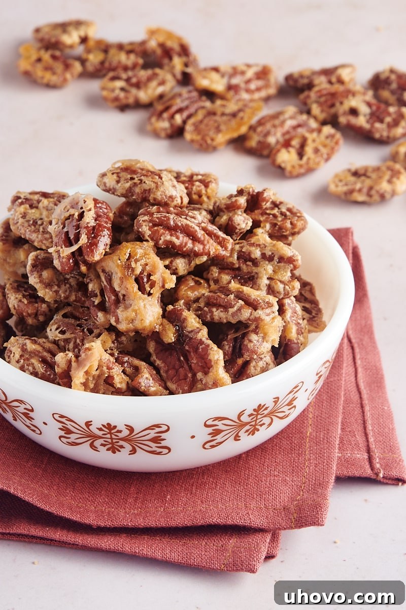 A bowl of glistening glazed pecans, with more pecans scattered in the background, highlighting their sweet and crunchy texture.