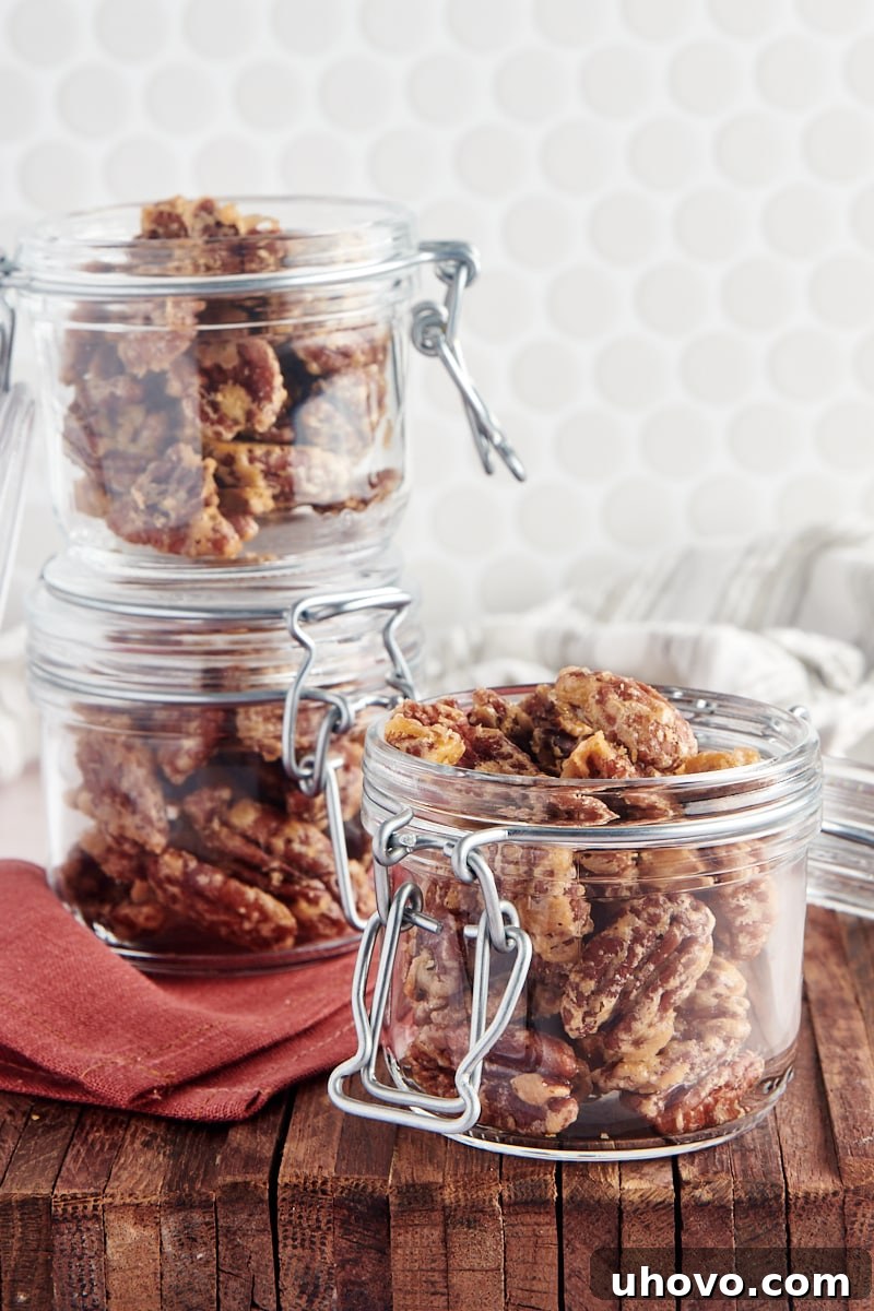 Three clear glass jars filled to the brim with golden, shiny Glazed Pecans, ready for storage or gifting.
