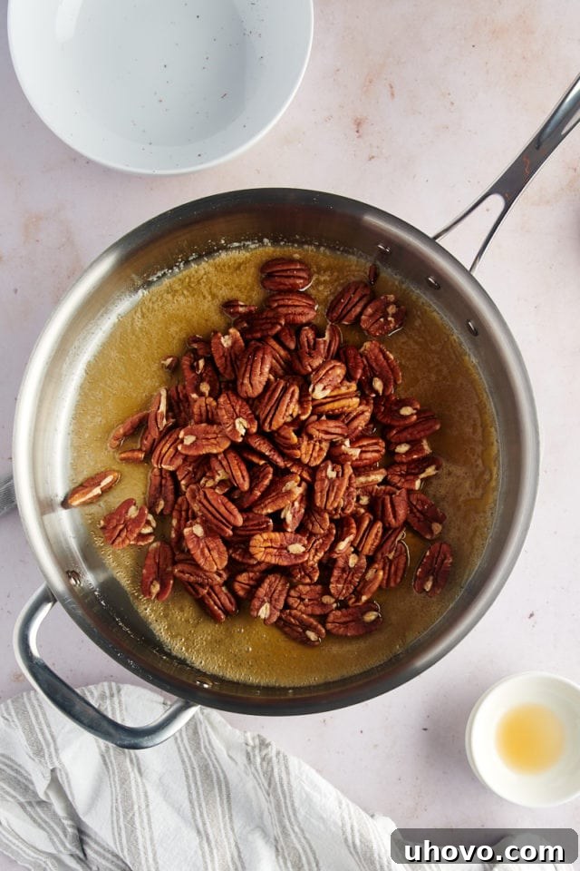 Pecan halves being stirred into the bubbling glaze mixture in a skillet, ensuring an even coating.