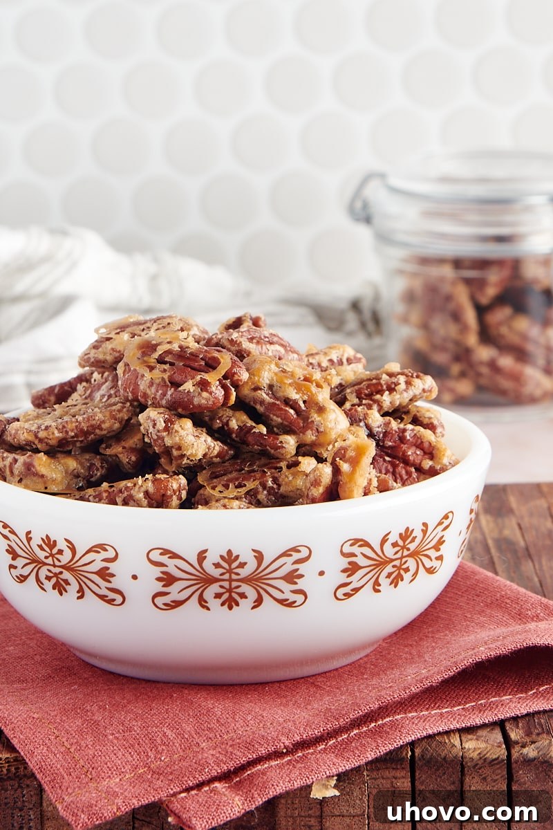A close-up, side view of golden Glazed Pecans piled high in a white bowl, showcasing their crunchy texture and sweet coating.