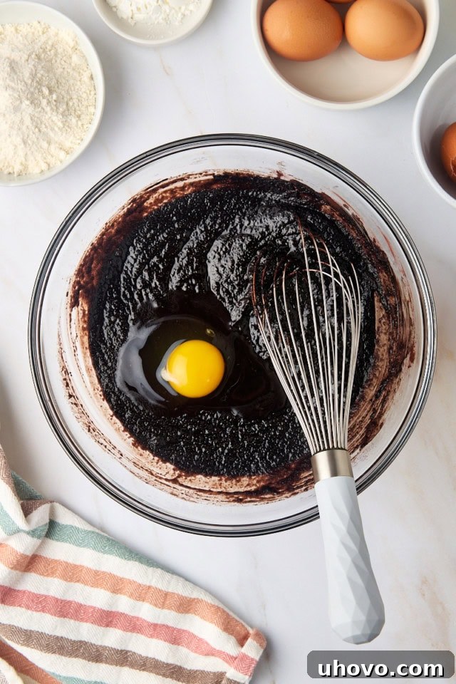 overhead view of egg added to brownie batter in a glass mixing bowl