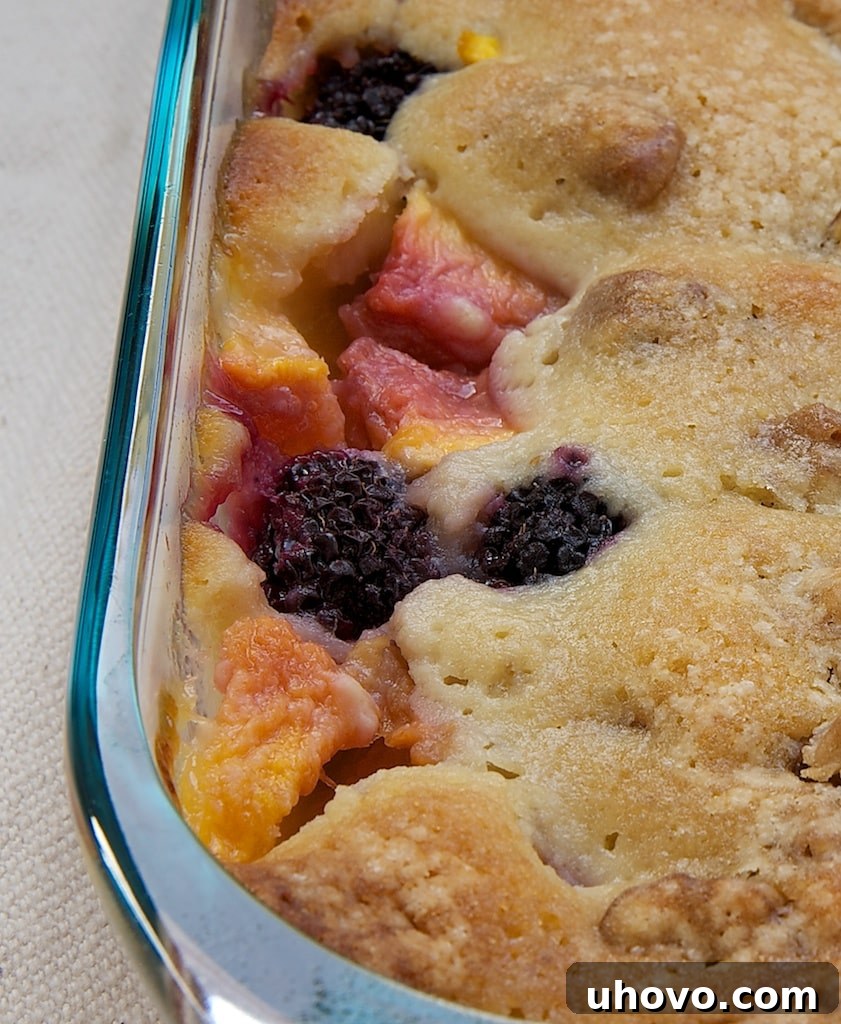 Blackberry Peach Cobbler baking in a clear glass dish, showcasing the fruit and topping