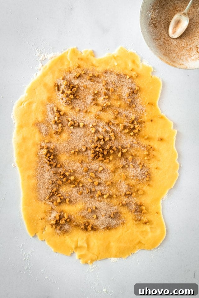 Cookie dough rectangle topped evenly with the pecan and cinnamon sugar mixture, ready for rolling.