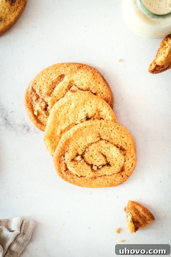 Three perfectly baked cinnamon roll cookies arranged on a marble slab, showcasing their golden color and intricate cinnamon swirls.