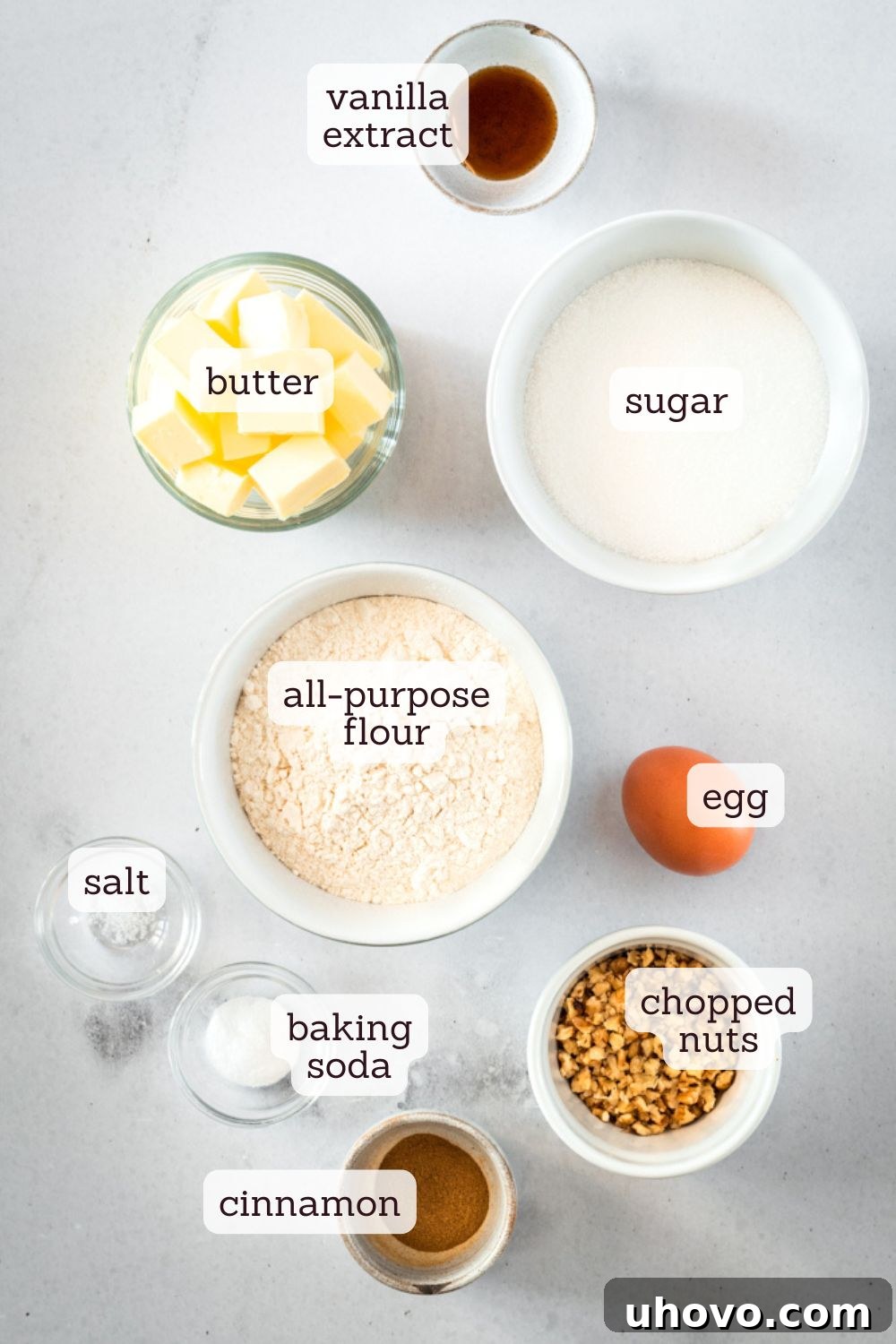 Overhead view of various baking ingredients, including flour, sugar, butter, eggs, pecans, and cinnamon, neatly arranged on a countertop, ready for making cinnamon roll cookies.