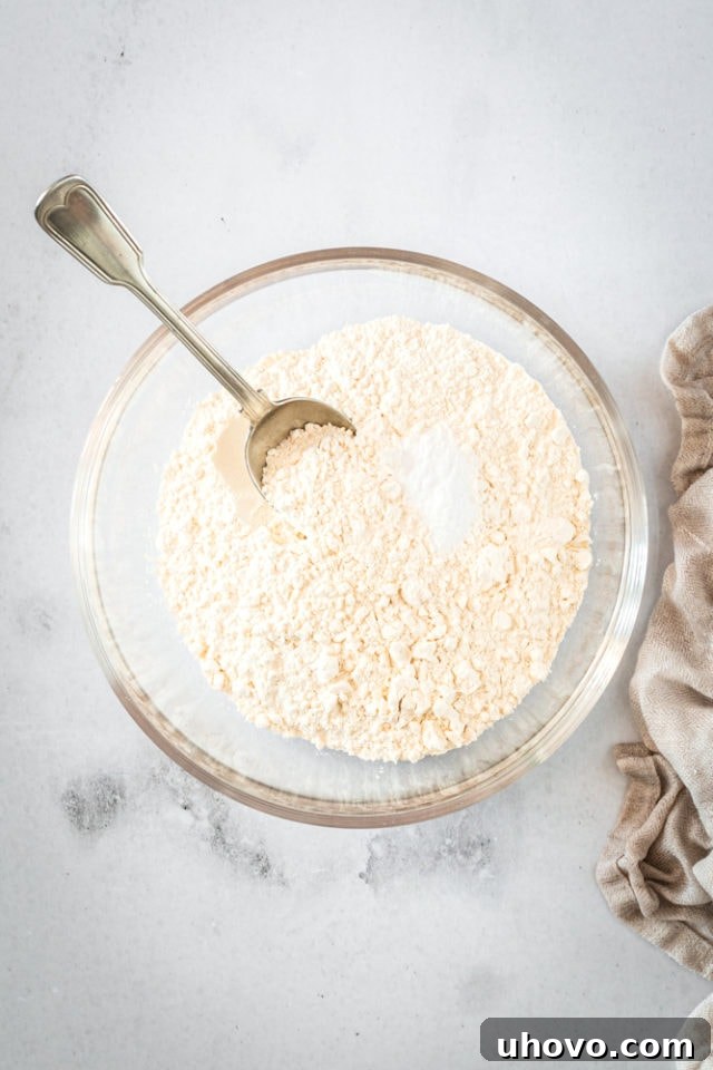 Overhead shot of dry ingredients for cookies in a glass bowl with a spoon, highlighting the flour, baking soda, and salt.