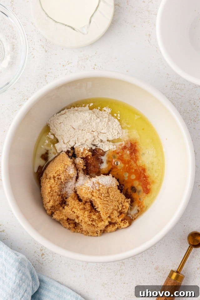 overhead view of brown sugar, melted butter, flour, milk, salt, and vanilla in a white mixing bowl