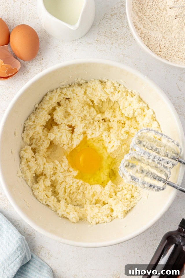 overhead view of egg added to creamed butter and sugar in a white mixing bowl