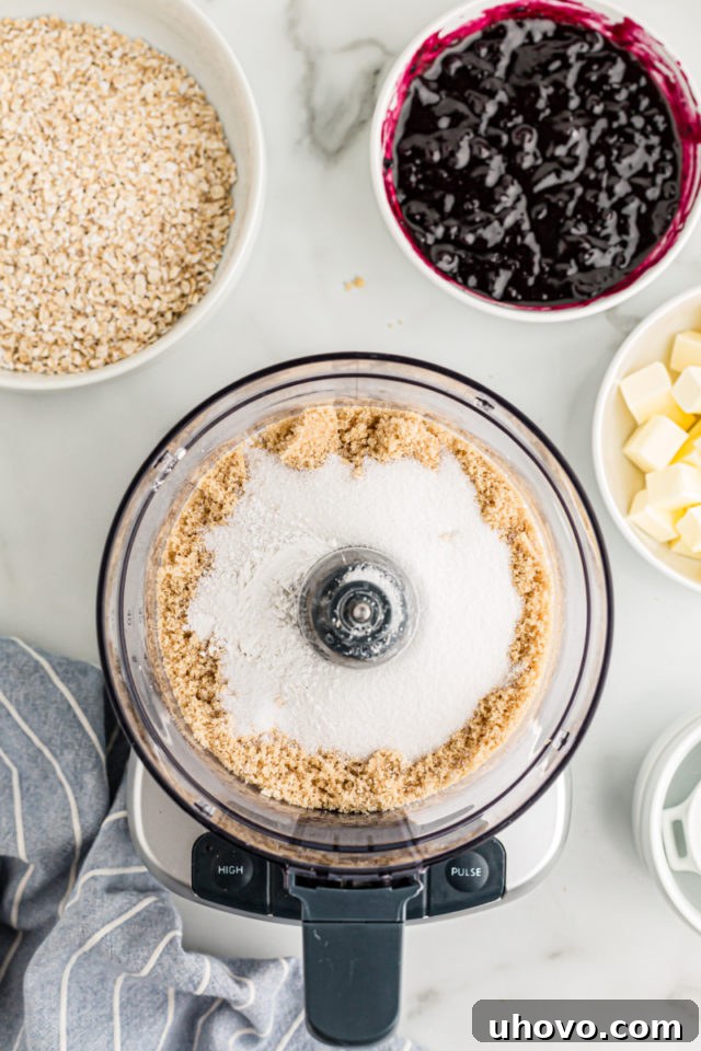 Overhead view of crust ingredients in food processor and blueberry jam in bowl