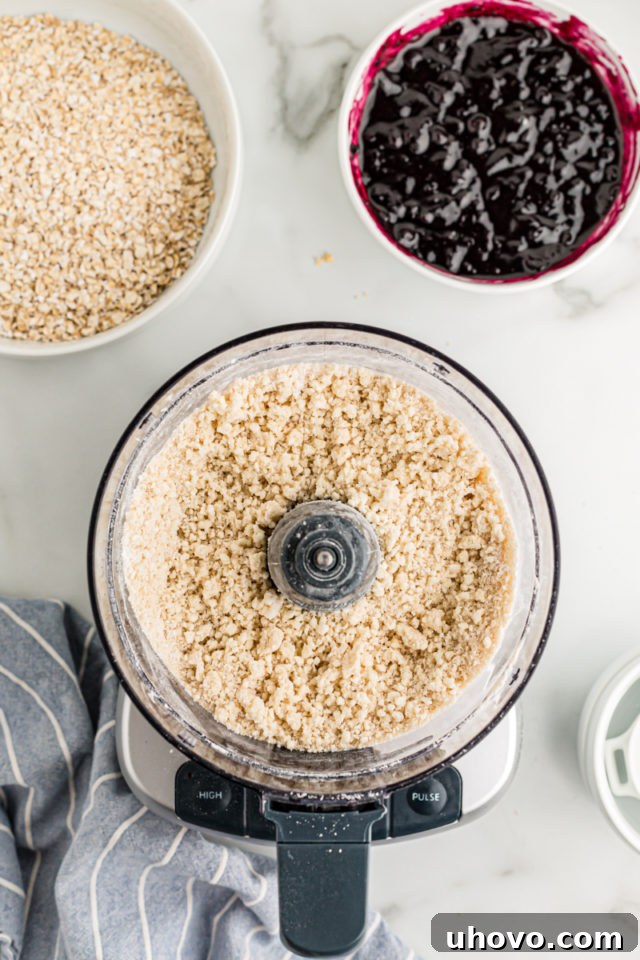 Overhead view of crust ingredients in food processor and blueberry jam in bowl