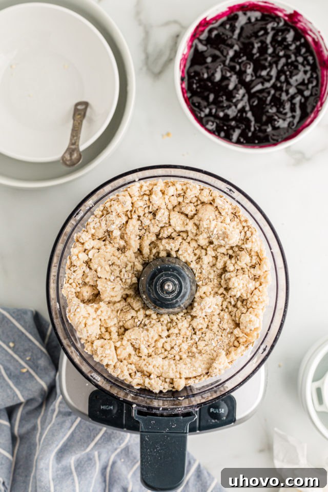 Overhead view of crust mixture in food processor and blueberry jam in bowl