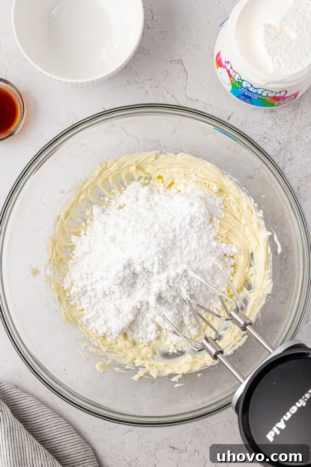 overhead view of confectioners' sugar added to creamed butter in a glass mixing bowl