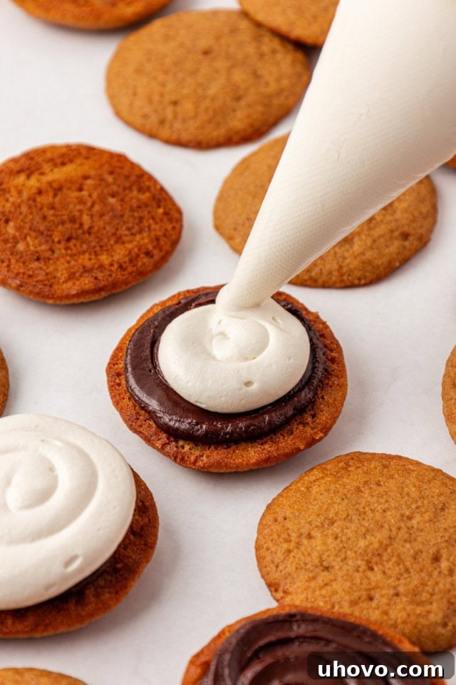 marshmallow buttercream being piped onto chocolate ganache spread on the bottom of a graham cake