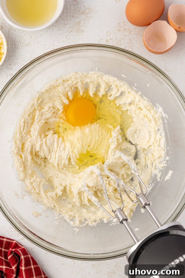 Overhead view of an egg being added to creamed butter and sugar in a glass mixing bowl, showcasing the fluffy and pale texture achieved through proper creaming.