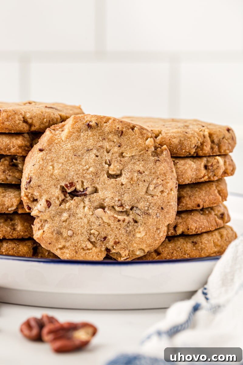 Stacks of pecan sandies on a plate, with one cookie on its side. These classic pecan cookies practically melt in your mouth!