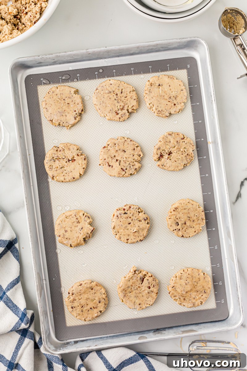Overhead view of unbaked pecan sandies on a baking sheet, flattened slightly before baking.