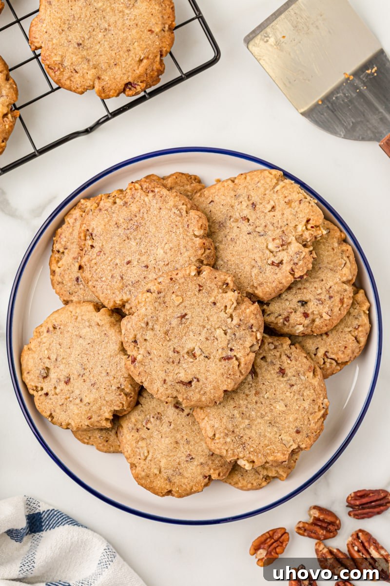 Overhead view of pecan sandies perfectly stacked on a white plate, ready for serving. These classic pecan cookies practically melt in your mouth!
