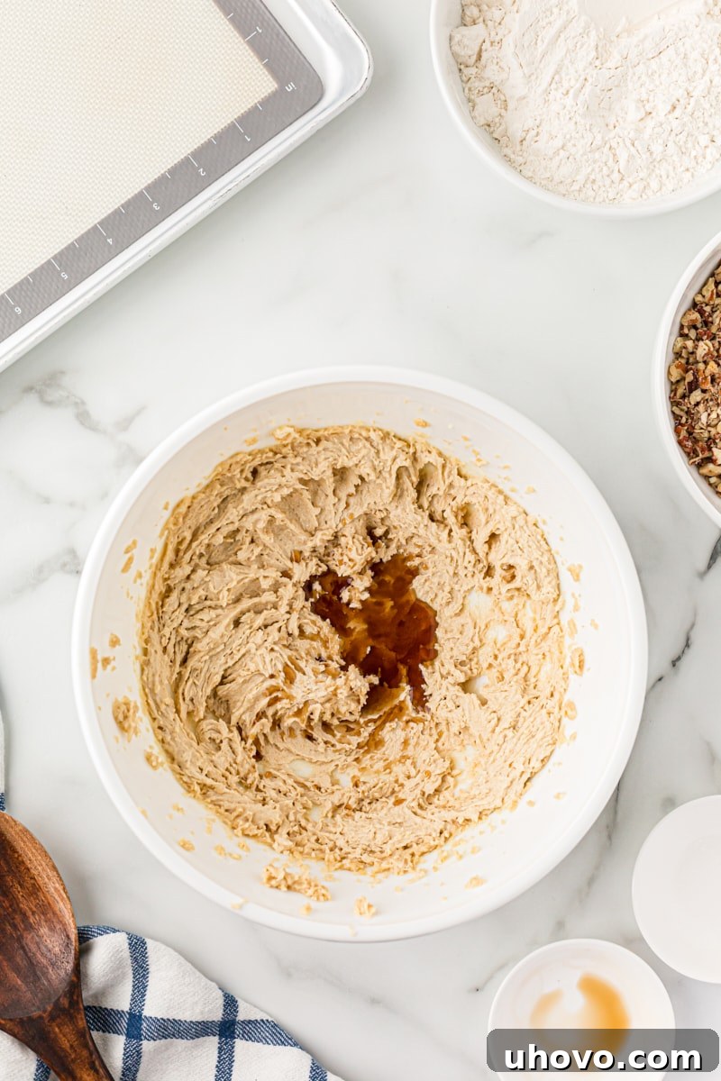 Overhead view of vanilla extract being added to a bowl of creamed butter and sugar, forming the base for pecan sandies dough.
