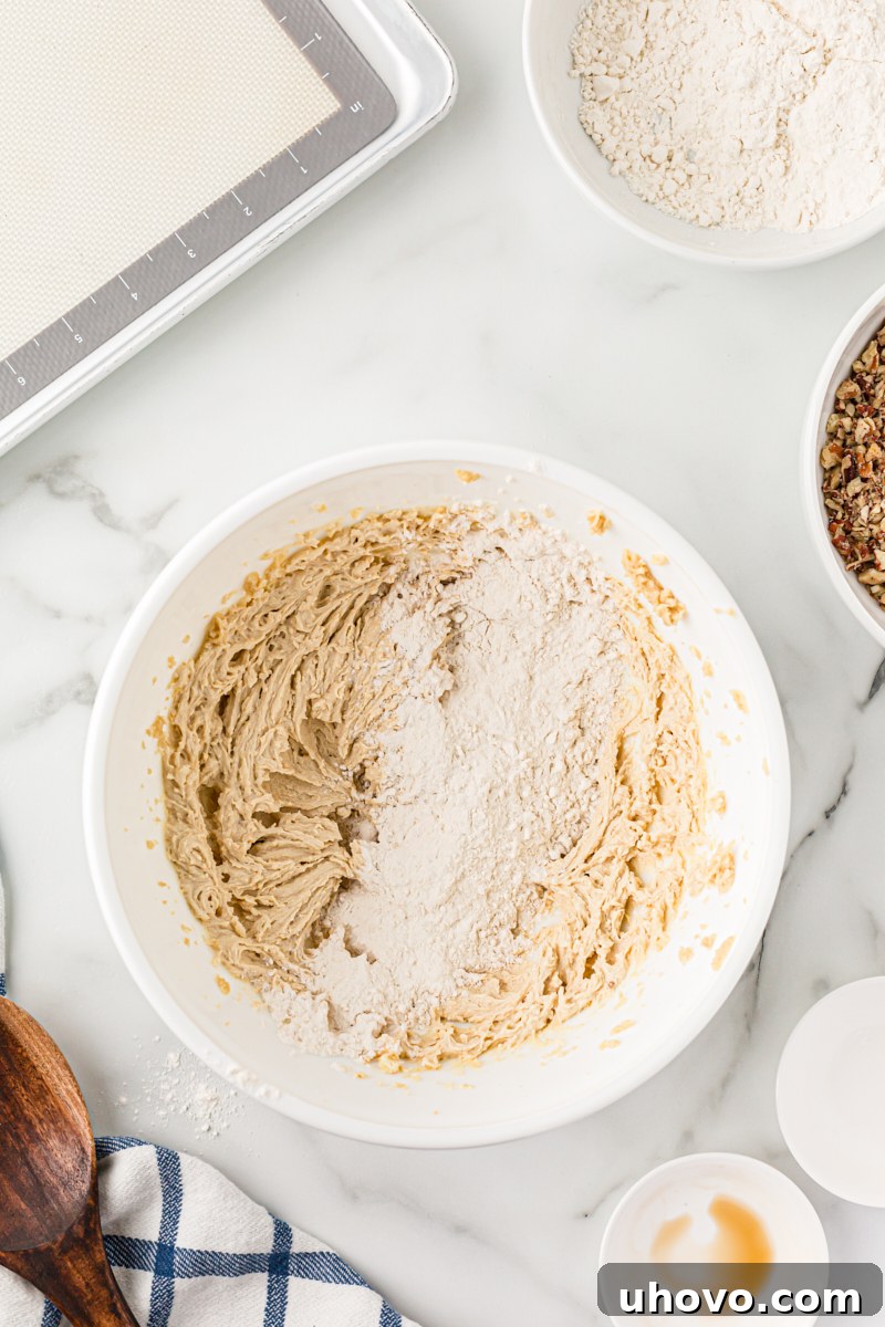 Overhead view of dry ingredients (flour) being added gradually to the butter and sugar mixture for pecan sandies dough.