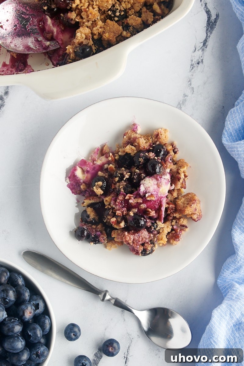 Overhead view of a single serving of blueberry crisp on a plate, next to a spoon, showing the layers clearly.