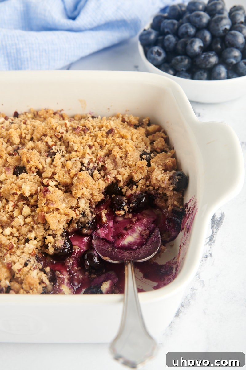 A baking dish of blueberry crisp with one portion already removed, showcasing the layers.