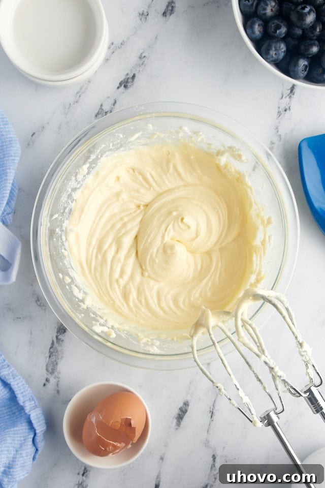 Overhead view of cream cheese layer being beaten smooth in a mixing bowl with electric beaters.