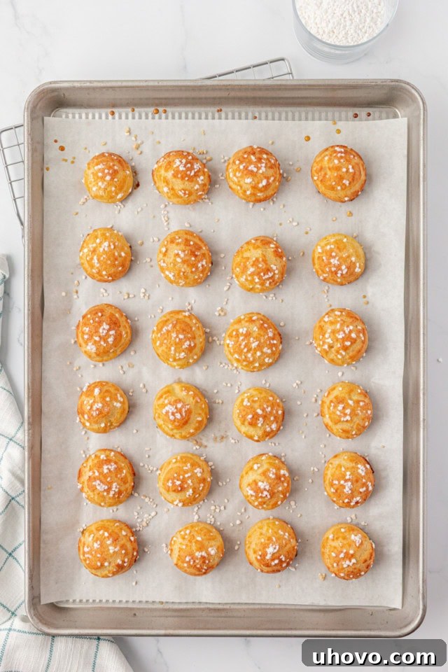 overhead view of a baking sheet filled with freshly baked, golden brown chouquettes, perfectly puffed and topped with sparkling pearl sugar, cooling slightly after being removed from the oven