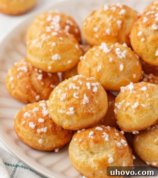 golden chouquettes topped with pearl sugar, stacked on a white plate
