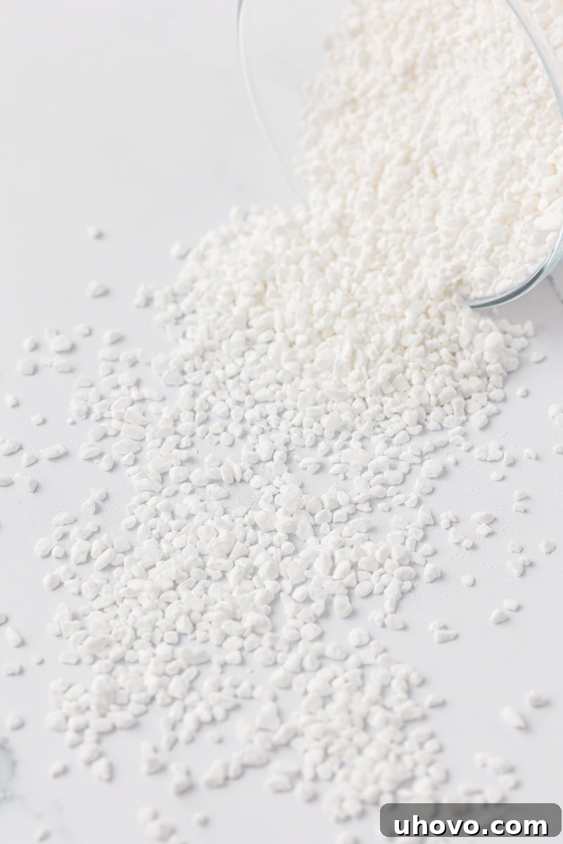 Pearl sugar spilled out of a clear jar onto a white surface, showcasing its distinct coarse texture and crystalline sparkle, ready to be sprinkled on pastries.