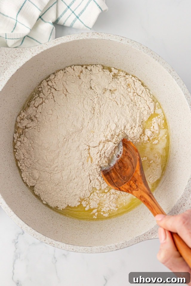 overhead view of all-purpose flour being added rapidly to the simmering liquid mixture in a saucepan, creating a cloud of dust as it hits the hot butter and milk