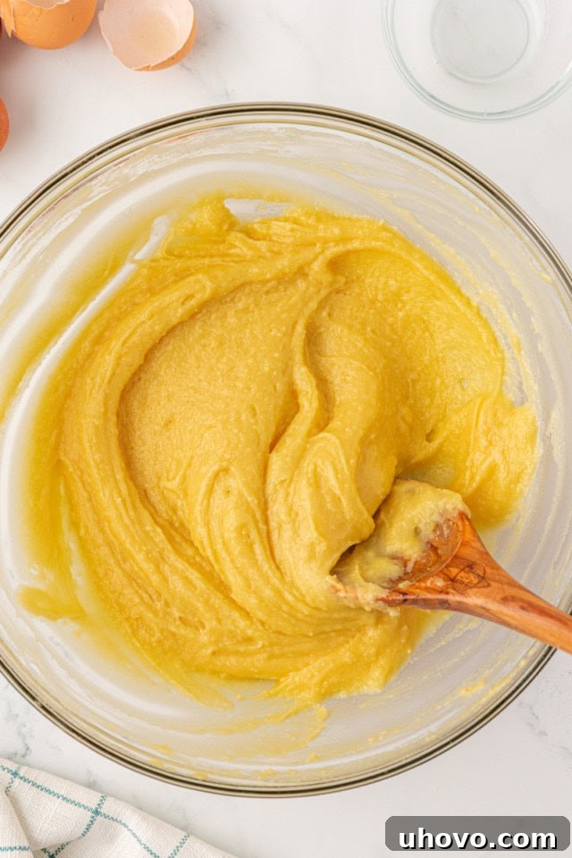 overhead view of thoroughly mixed choux pastry dough in a glass mixing bowl, displaying a smooth, thick, and glossy consistency, perfect for piping