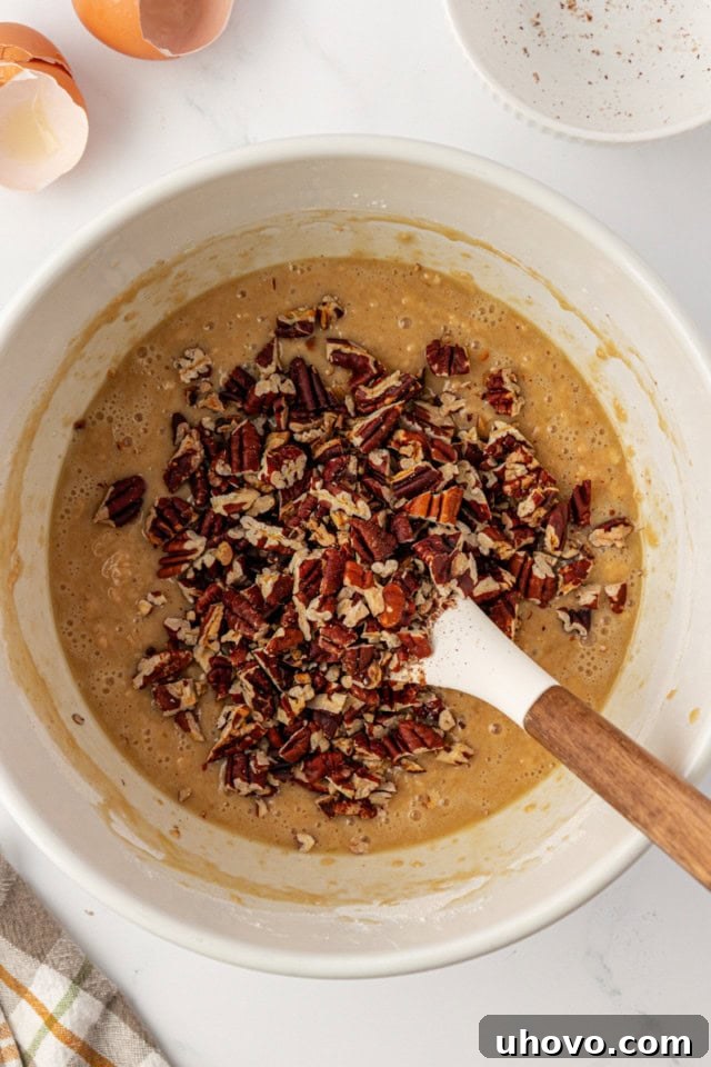 overhead view of chopped toasted pecans added to pecan praline muffin batter in a white mixing bowl