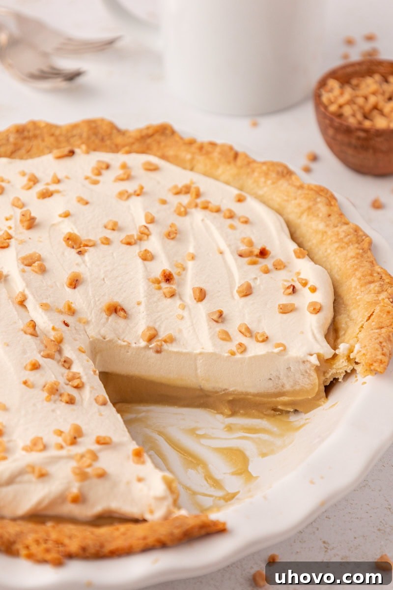 butterscotch pie topped with brown sugar whipped cream in a white pie plate with two slices missing