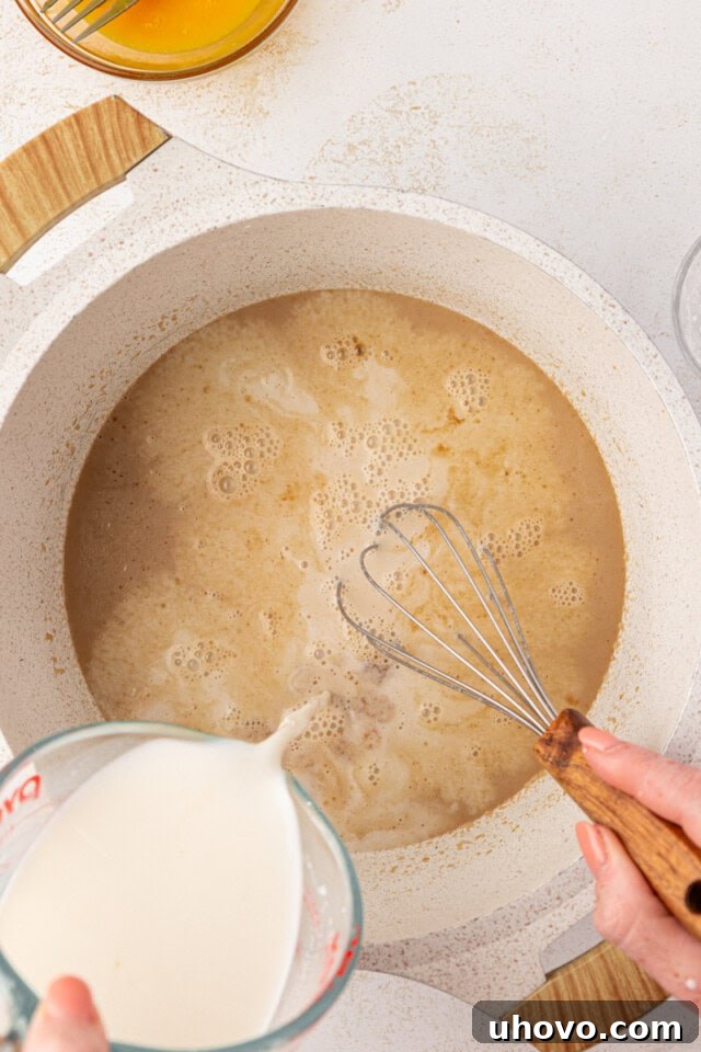 overhead view of milk being whisked into melted butter and brown sugar in a white saucepan