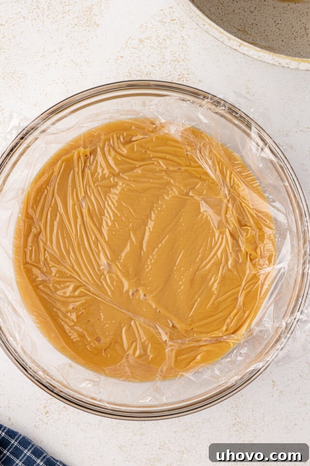 overhead view of butterscotch pie filling covered with plastic wrap in a glass bowl