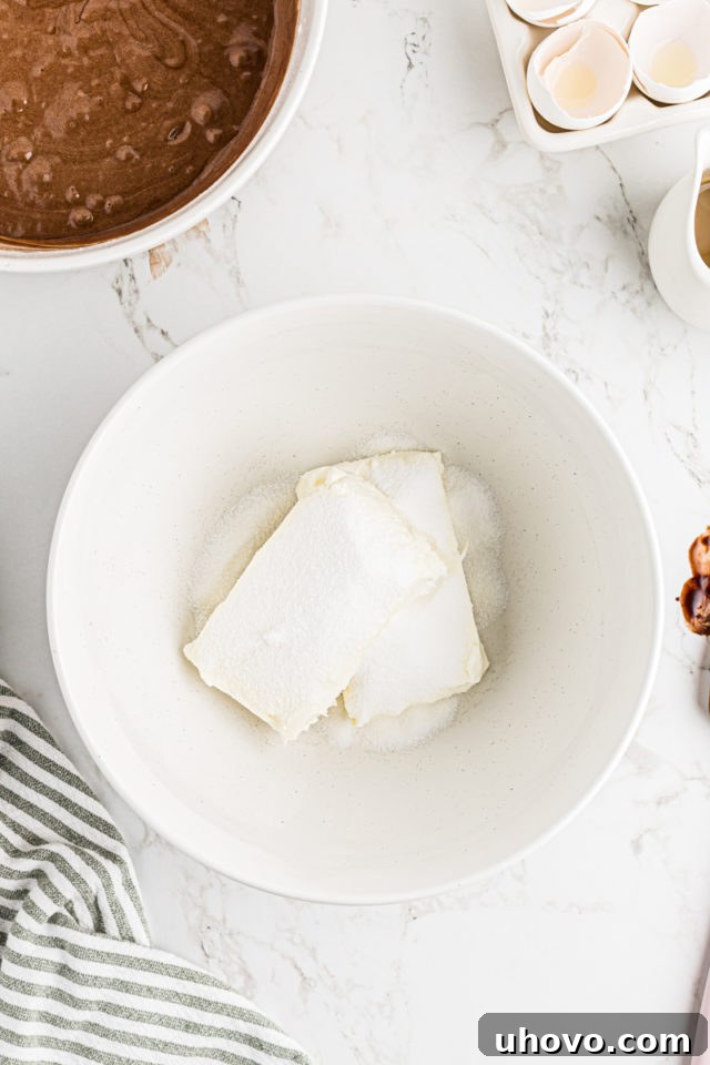 Overhead view of cream cheese and sugar in bowl, being beaten until creamy.